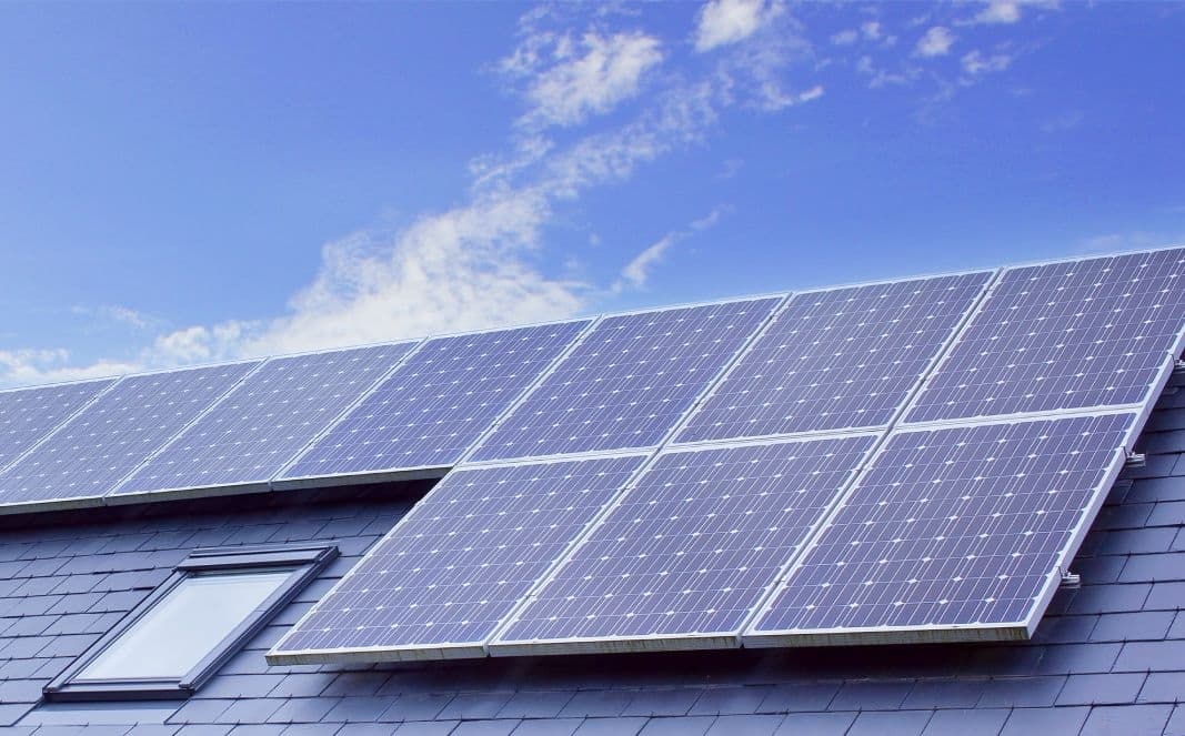 Two installers in hi-vis vests and hard hats fitting solar panels on a roof